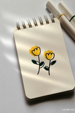 Um bloco de notas com dois desenhos simples de flores amarelas, acompanhados de dois marcadores, sobre uma superfície clara.