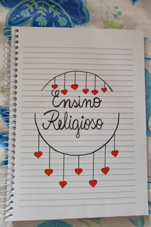 Uma página de caderno intitulada "Ensino Religioso" com corações vermelhos pendurados sob o título, adornada com um desenho encantador na capa do caderno.