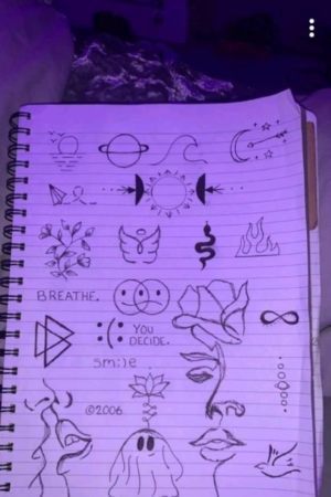 Página de caderno com vários esboços desenhados à mão, incluindo planetas, flores, rostos, símbolos e um fantasma dizendo "Boo!" na capa do caderno.