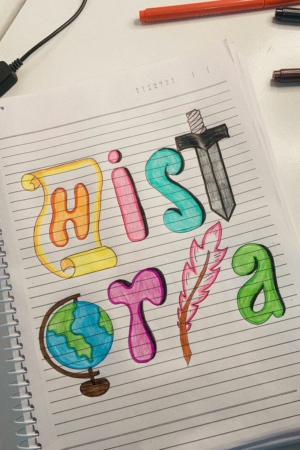 Letras coloridas "Historia" em papel pautado com desenho de uma espada, caneta de pena e globo, perfeitas para a capa do caderno.