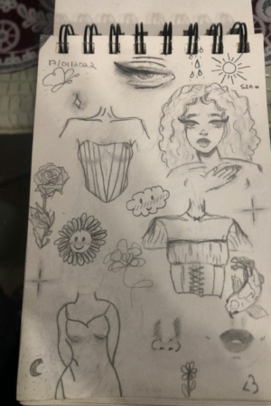 Uma página de caderno de desenho repleta de vários desenhos a lápis, incluindo uma mulher, flores, um espartilho, lábios e desenhos abstratos. Para desenhar.