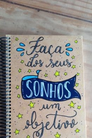 Um caderno espiral com uma capa vibrante onde se lê "Faça dos seus sonhos um objetivo", cercado por desenhos caprichosos de estrelas e pontos.